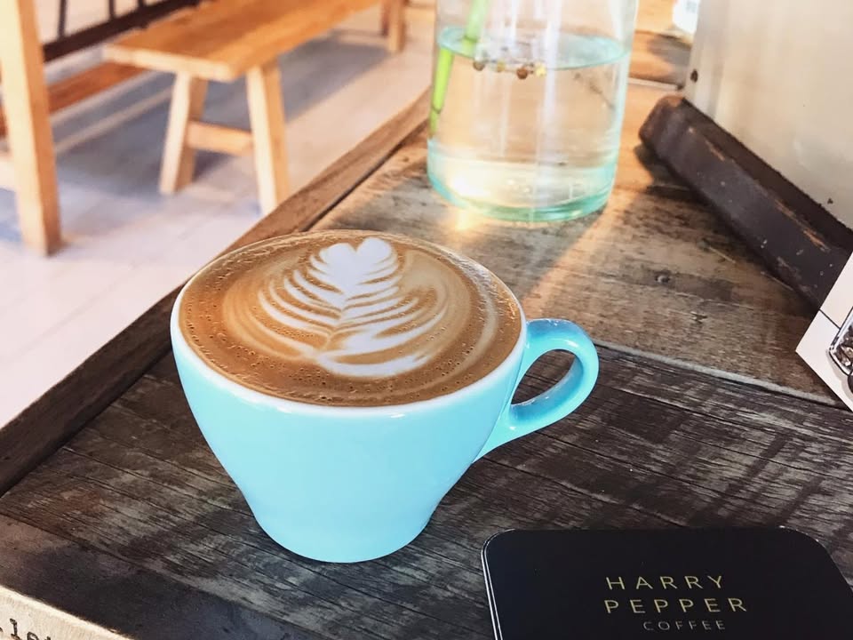 A flat white with rosetta latte art on a rustic timber tray