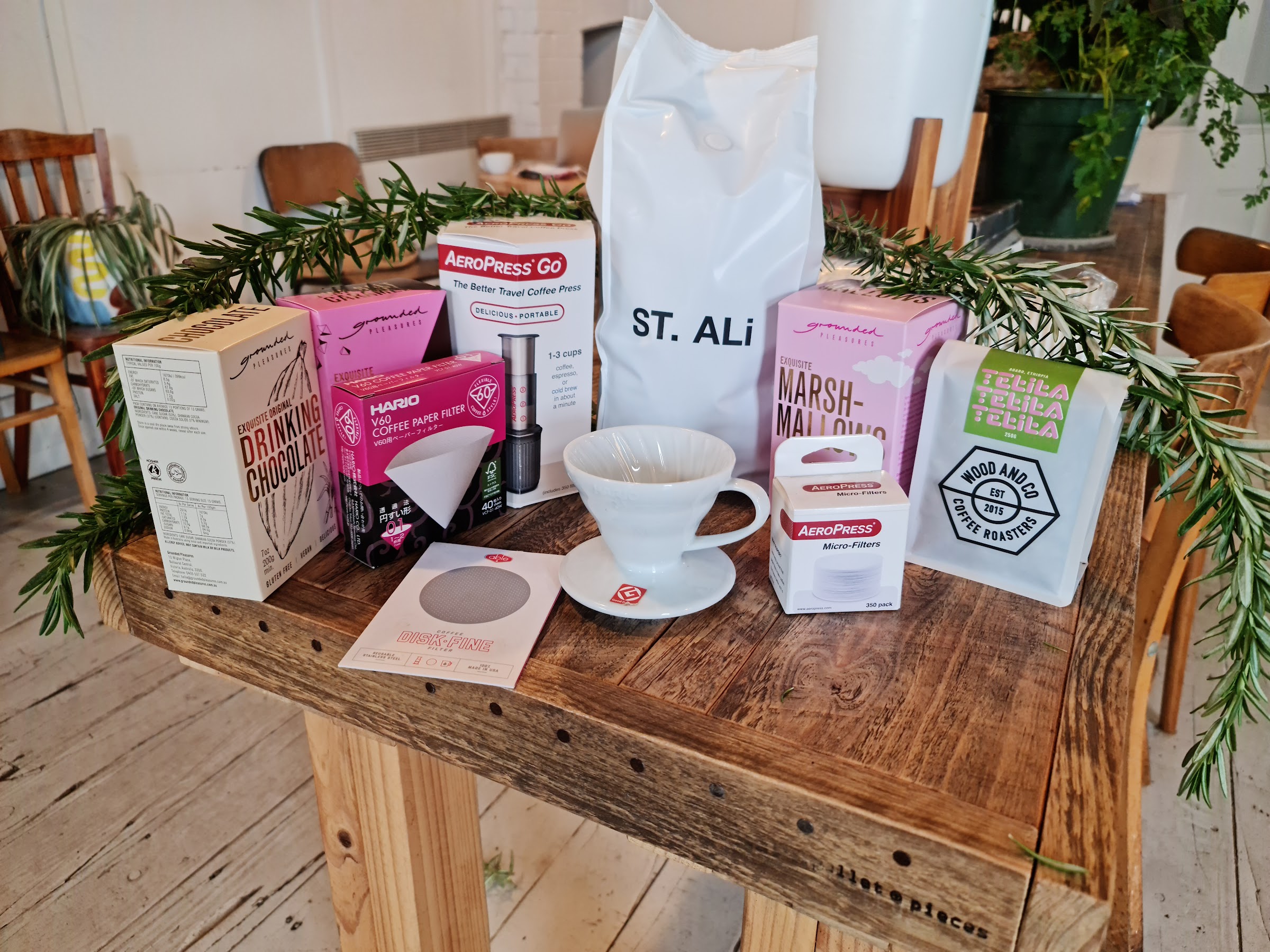 Bags of ST. ALi and Wood and Co coffee beans beside an AeroPress, a Hario V60 and drinking chocolate