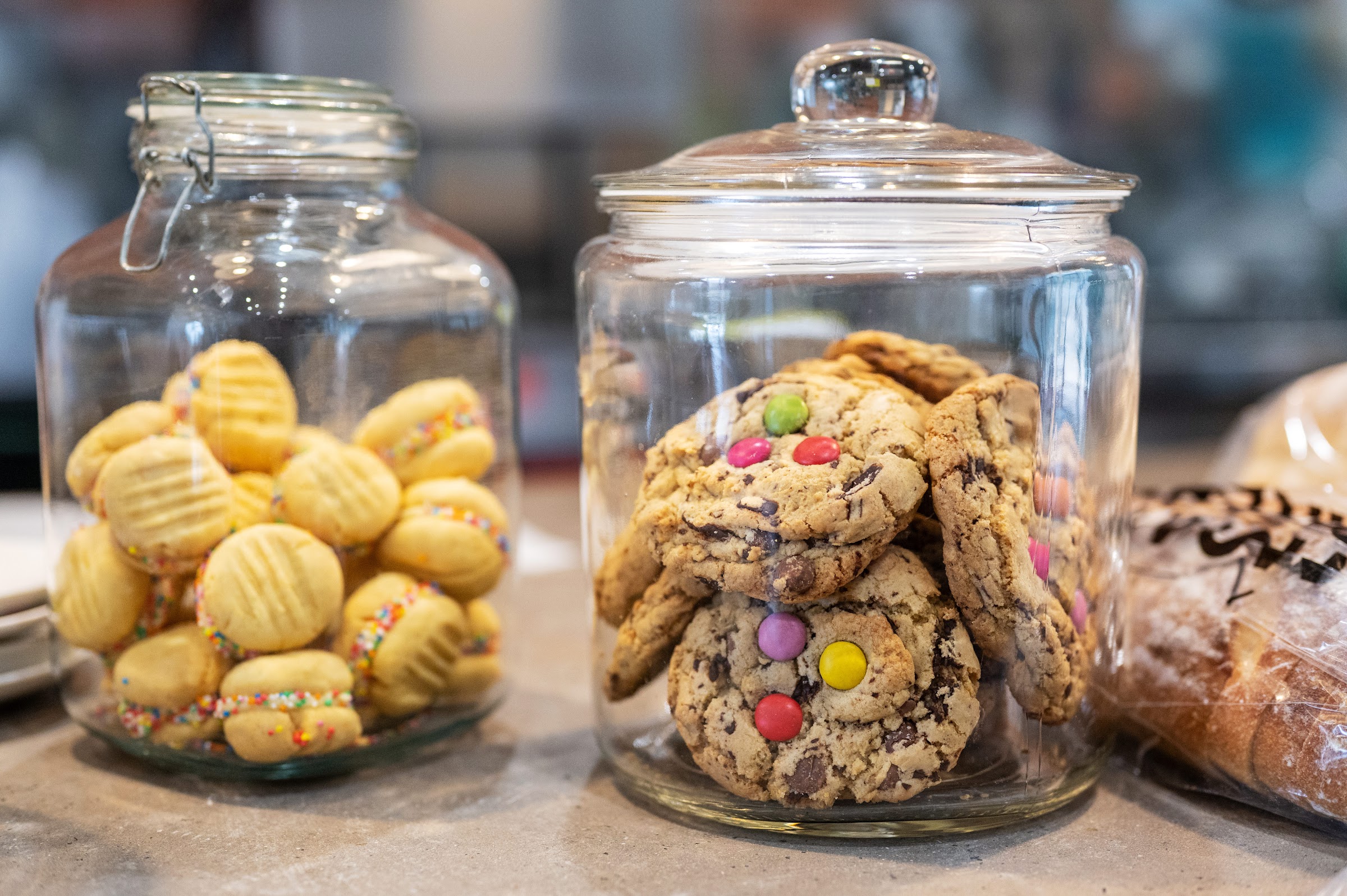 Two large glass jars of house biscuits and cookies beside a loaf of bread on the counter