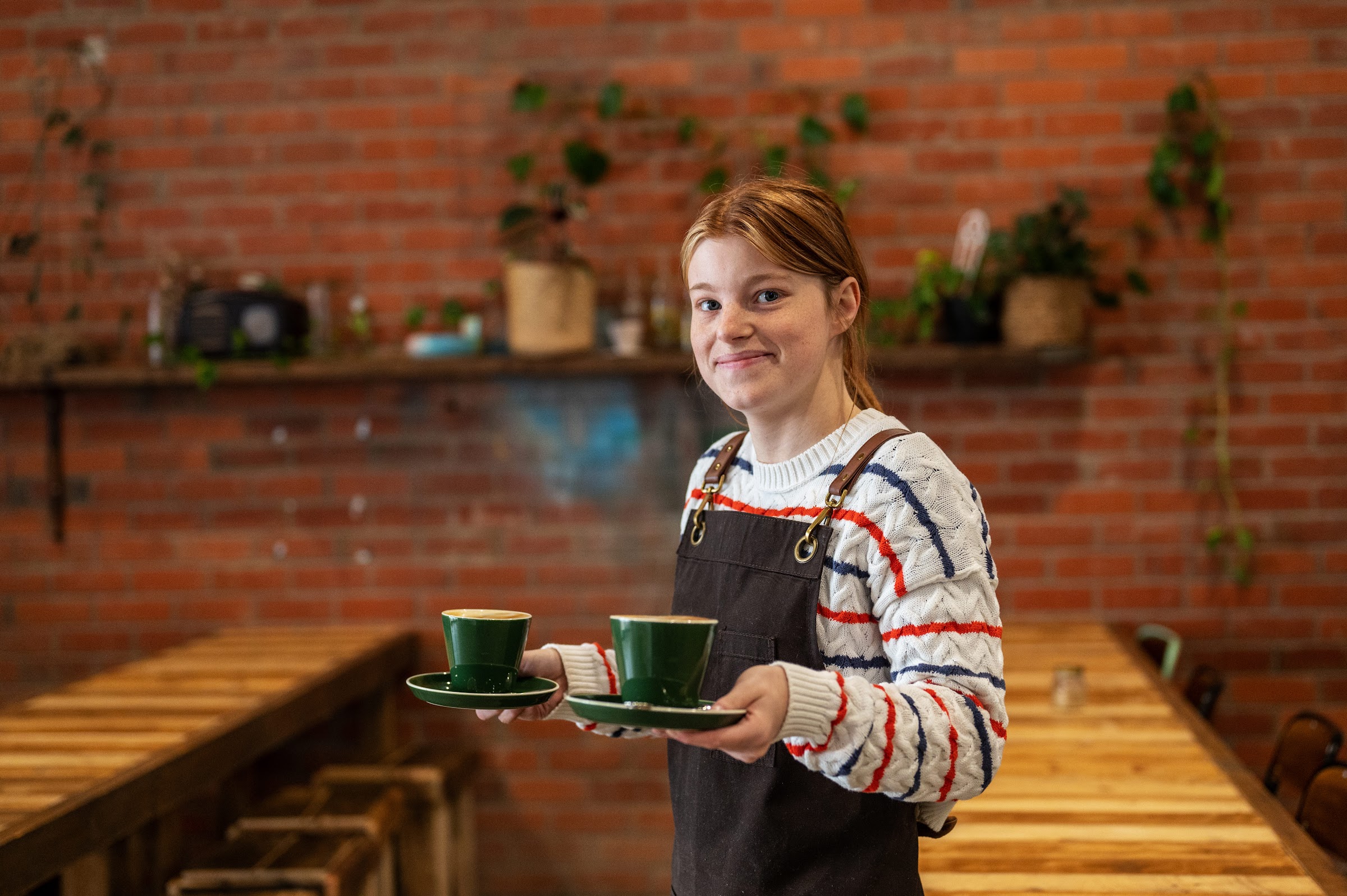 A staff member carrying two green cups and saucers past the exposed brick wall