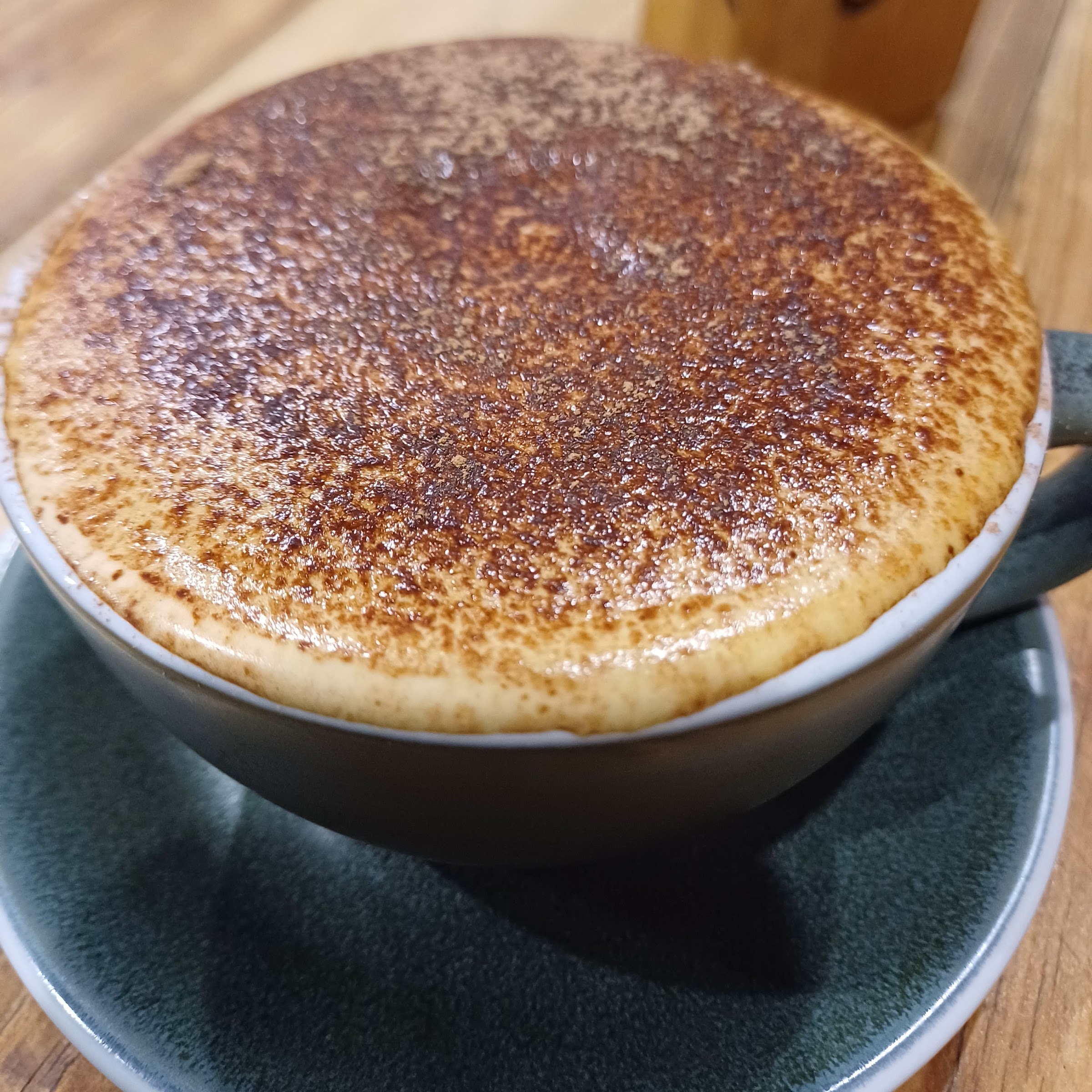 A cappuccino dusted with chocolate in a green cup at Harry Pepper Coffee