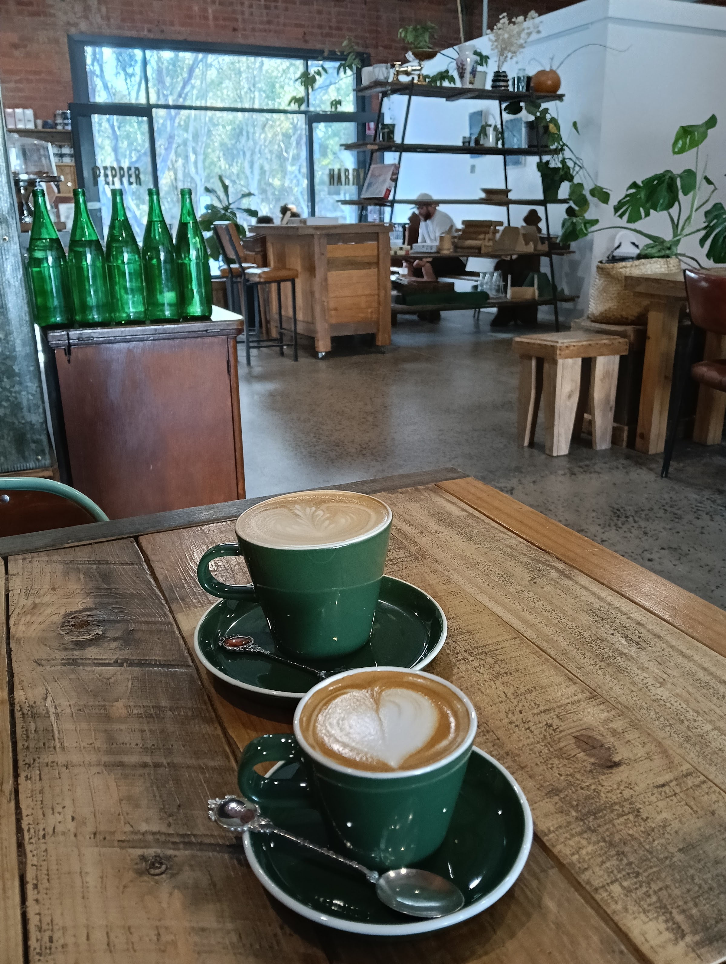 Two green cups of coffee with latte art on a reclaimed timber table inside Harry Pepper Coffee