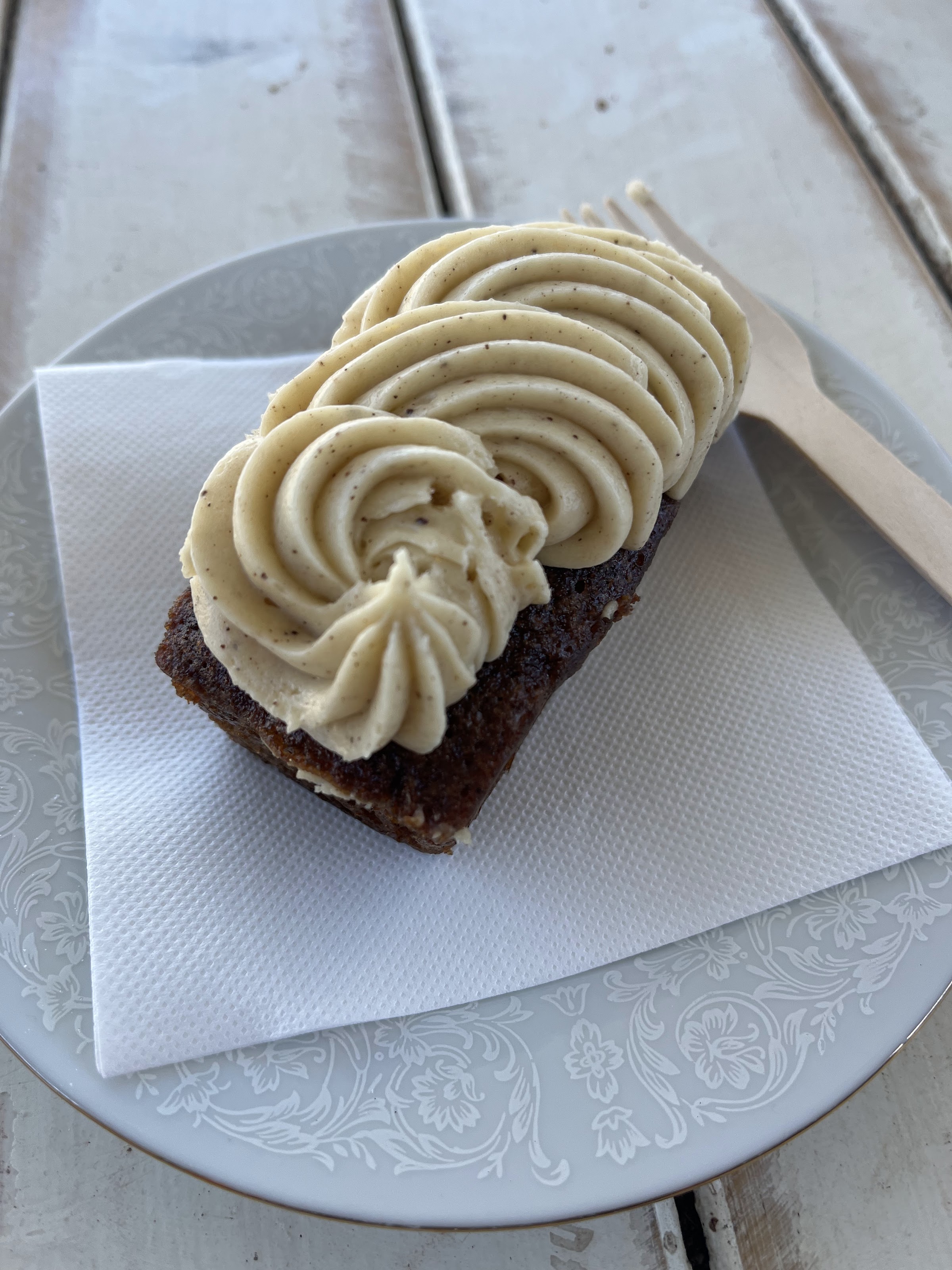 A slice of carrot cake topped with piped cream cheese frosting on a vintage plate